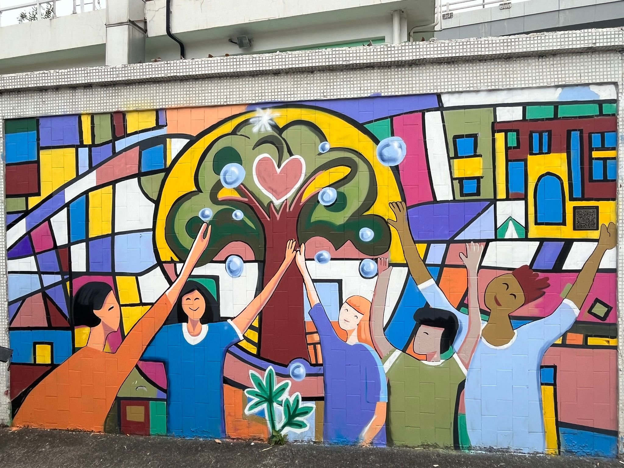 位於啟德4號旱流污水截流泵房部分外牆的壁畫 ─ 《Dragon城的多元生命值》，以5位不同族裔的青少年在象徵九龍城街道和棋盤的背景前歡聚交流，呈現了對社區和生命的美好願景