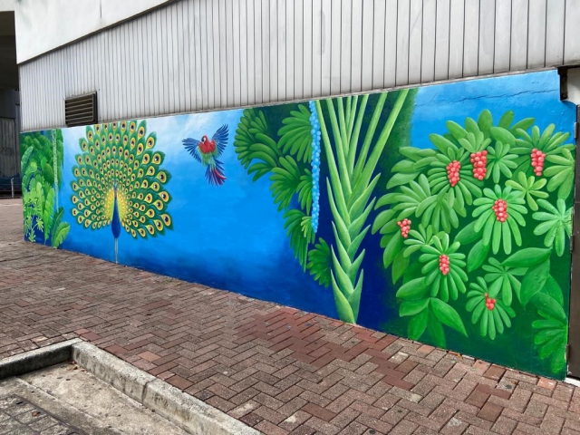 The sky-blue background is adorned with colourful macaws and an eye-catching peacock